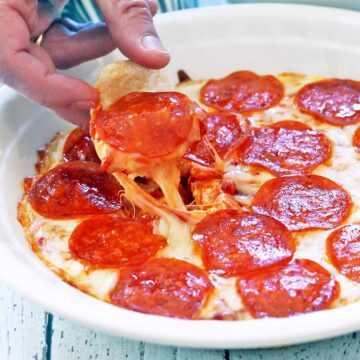 A hand scooping out pizza dip.