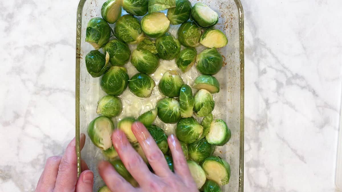 Mixing olive oil into Brussels sprouts. 