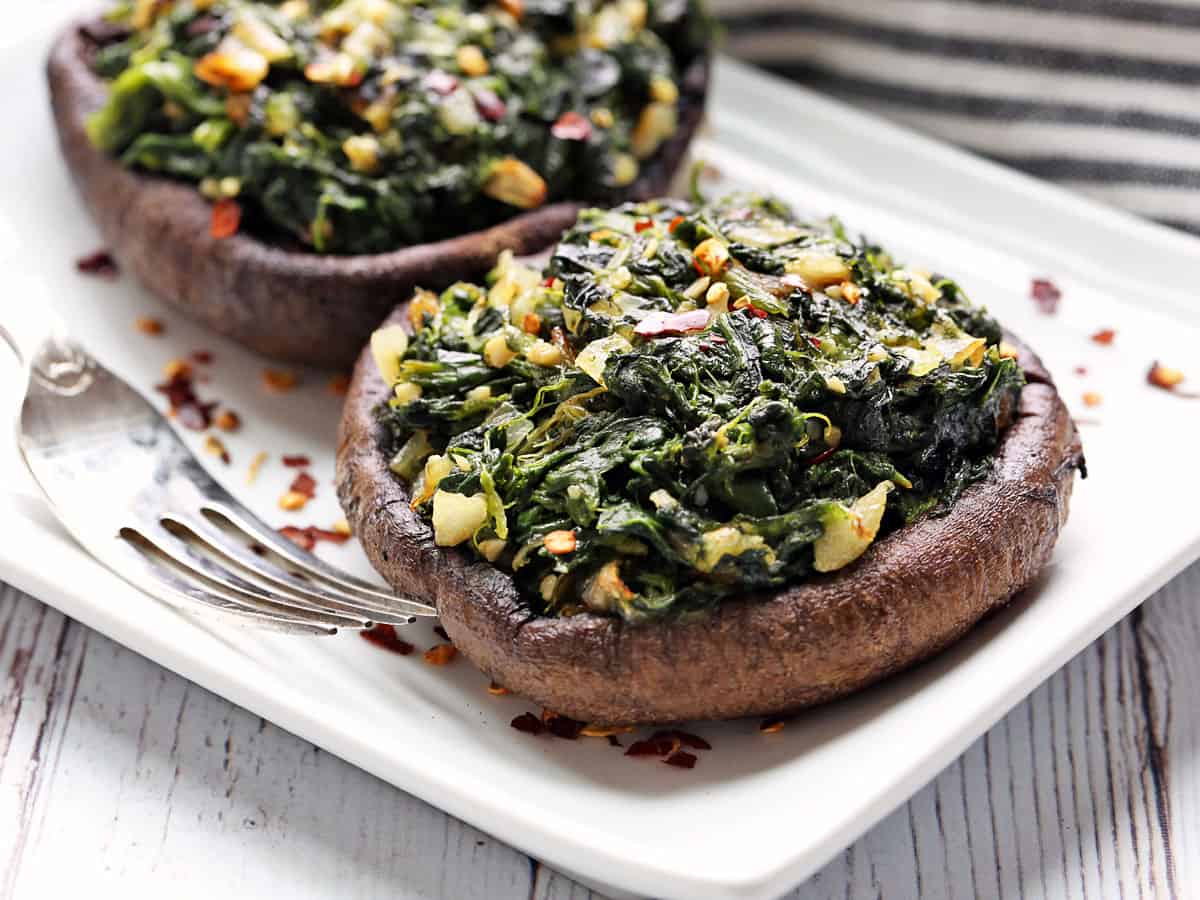 Stuffed portobello mushrooms are served on a white plate with a fork. 
