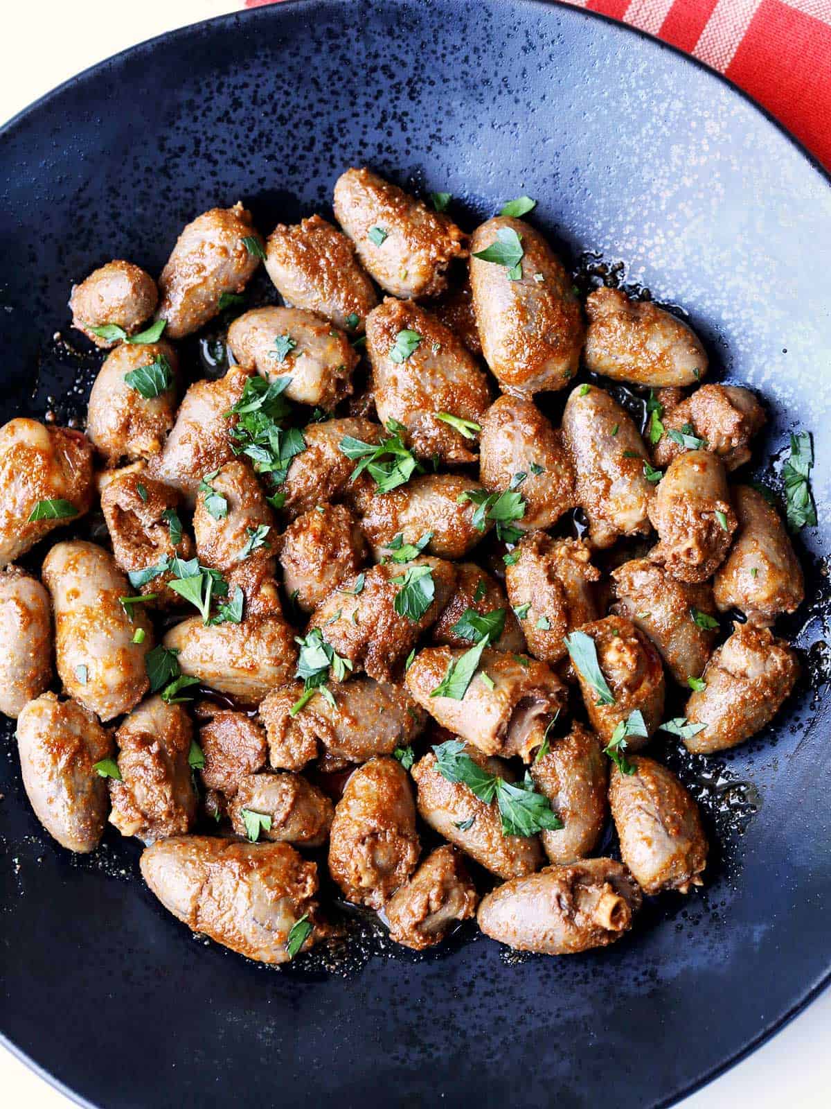 Chicken hearts are served on a dark plate and topped with parsley.