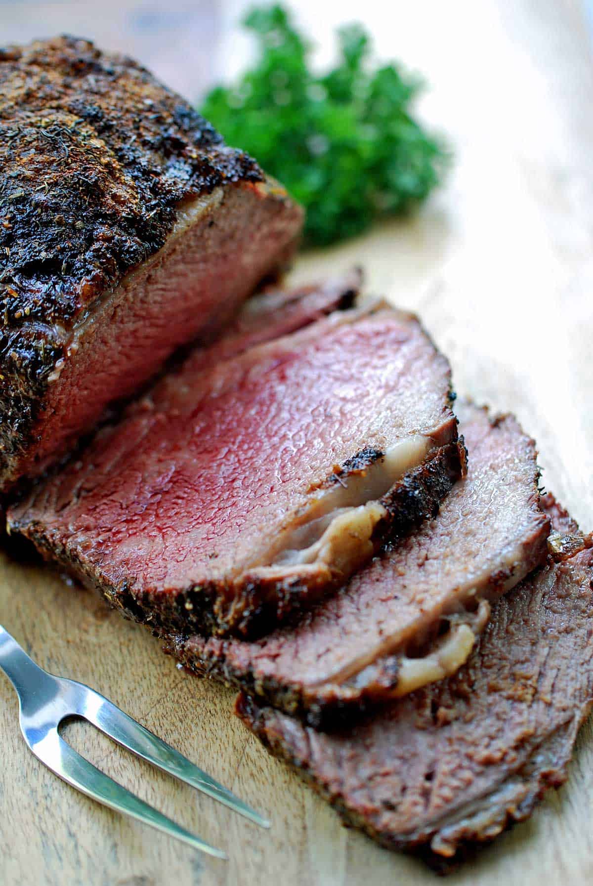 A ribeye roast served on a wooden cutting board with a garnish of parsley. 