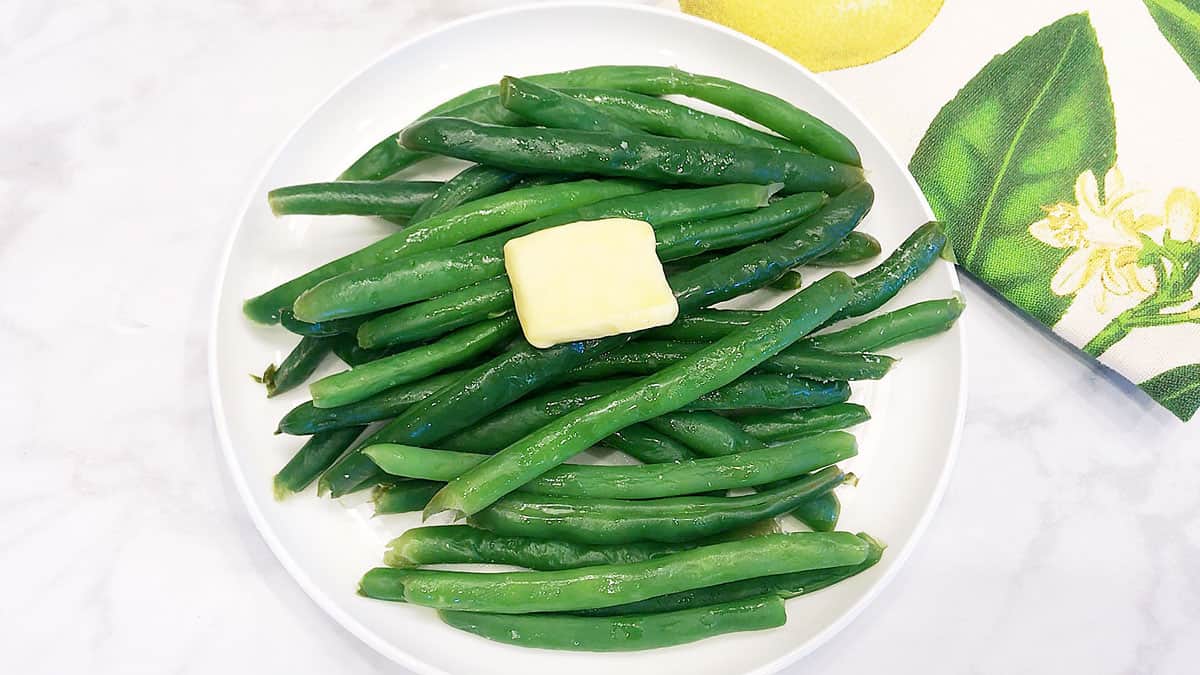 Green beans served on a white plate, topped with butter. 