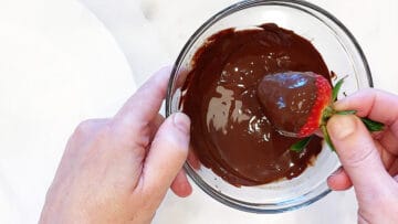 Dipping a strawberry in melted chocolate.