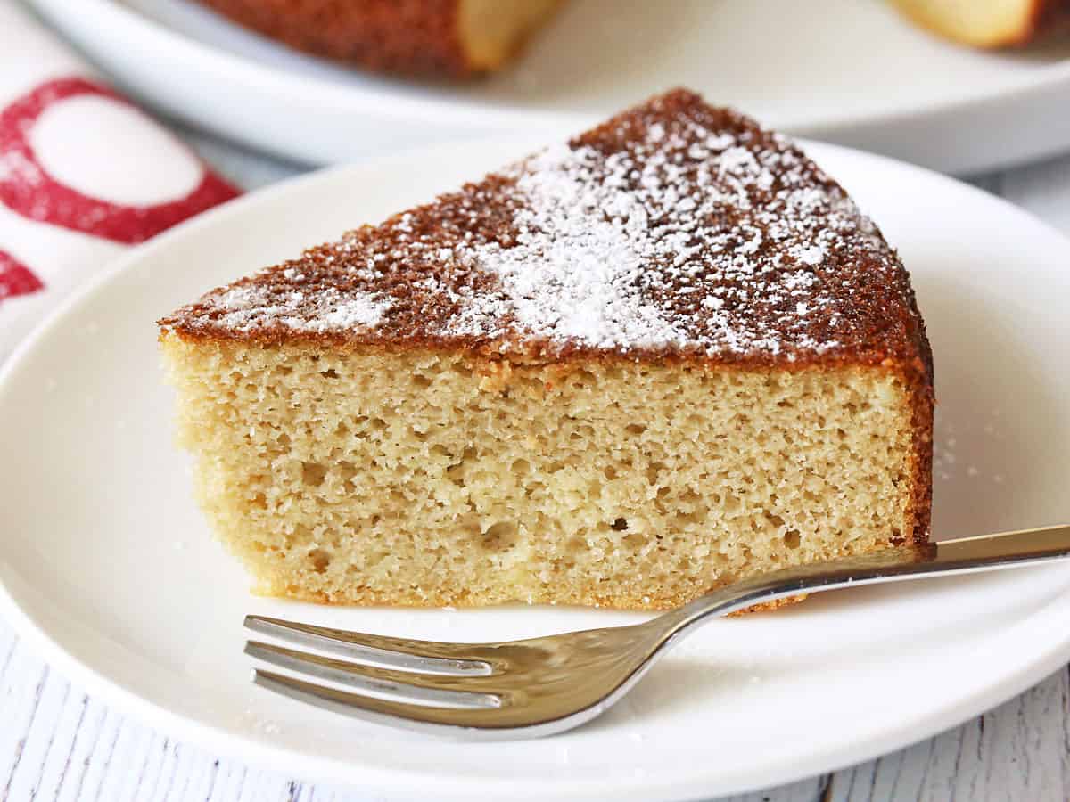 A slice of almond flour cake served on a white plate with a fork. 