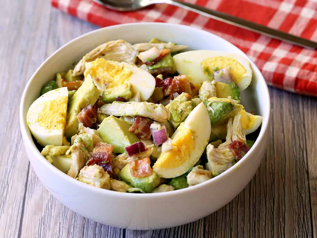 Avocado chicken salad served in a white bowl with a serving spoon. 