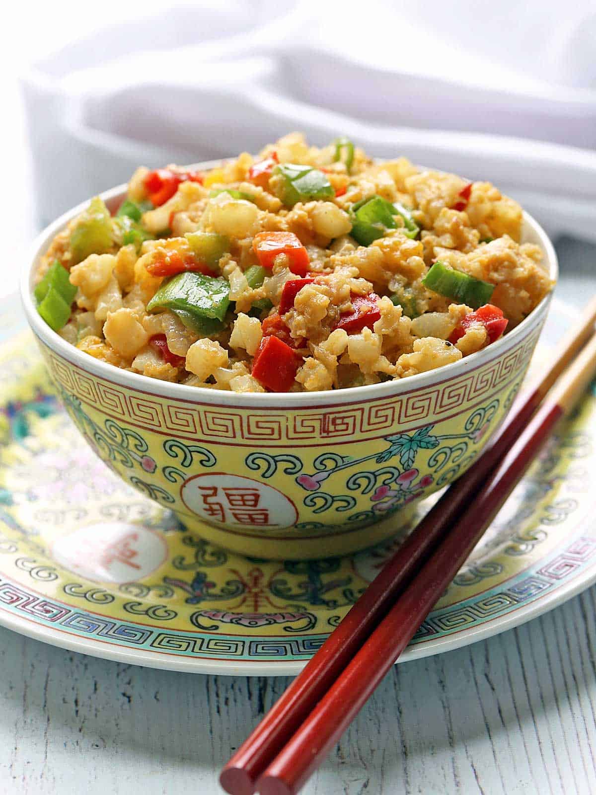 Cauliflower fried rice is served in a bowl with chopsticks. 