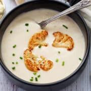 Cauliflower soup is served in a dark bowl with a spoon.