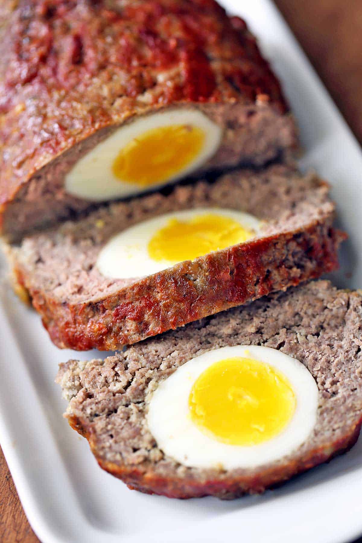 Egg-stuffed meatloaf, sliced, served on a white tray. 