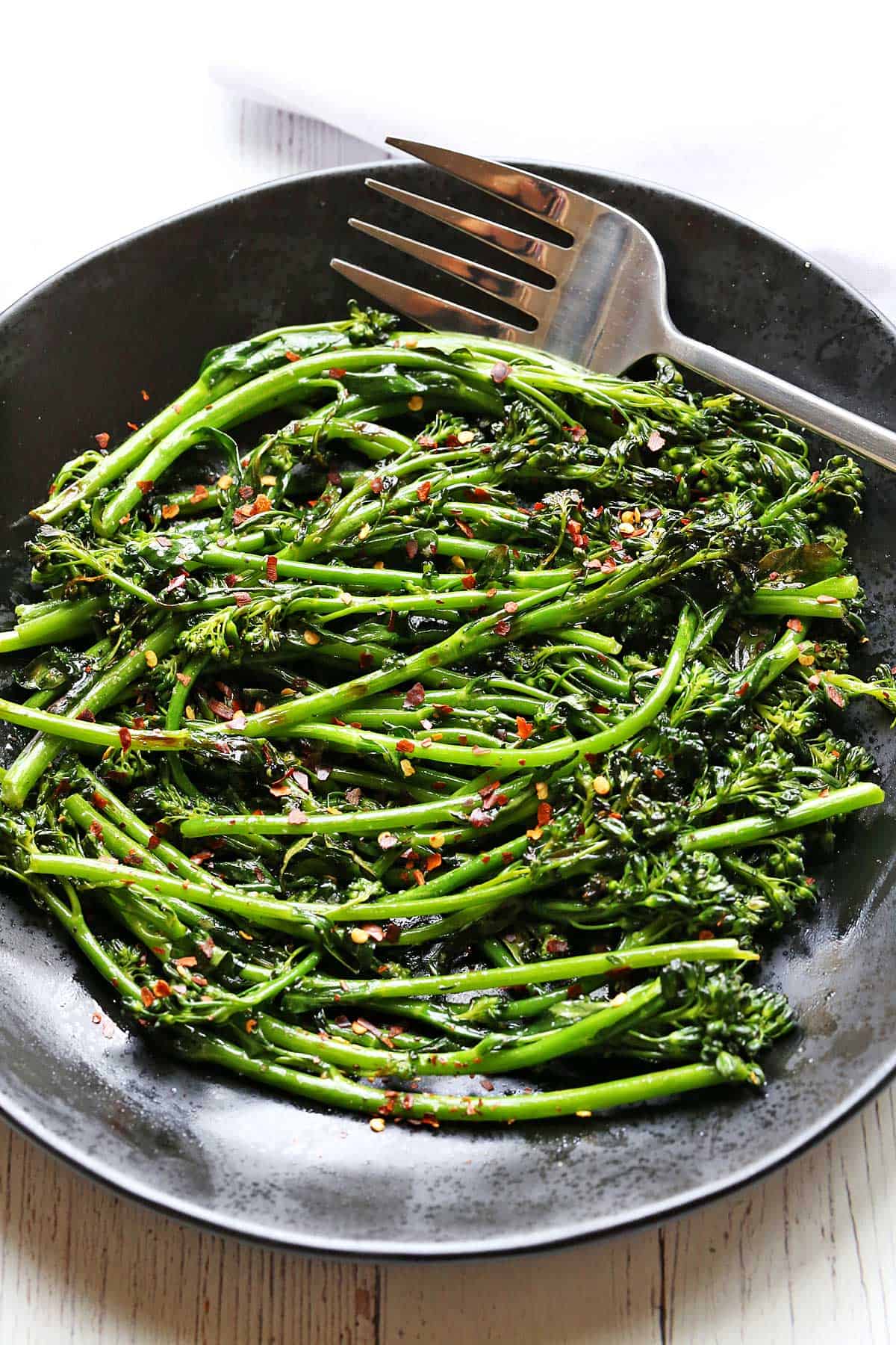 Grilled broccolini is served on a black plate. 