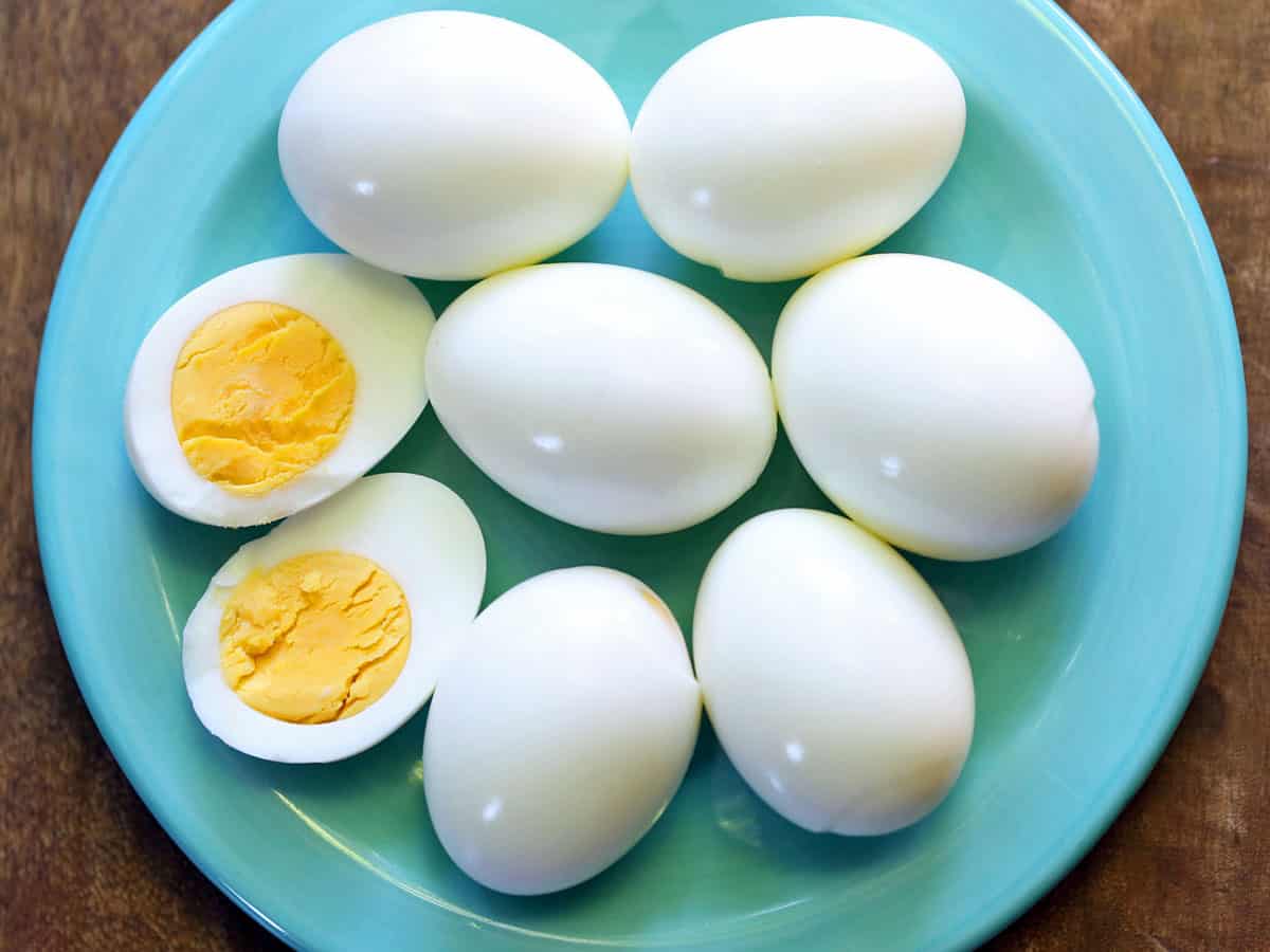 Seven peeled hard-boiled eggs served on a turquoise plate, one of them halved. 