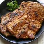 Pork shoulder steak is served on a dark plate with parsley for garnish.