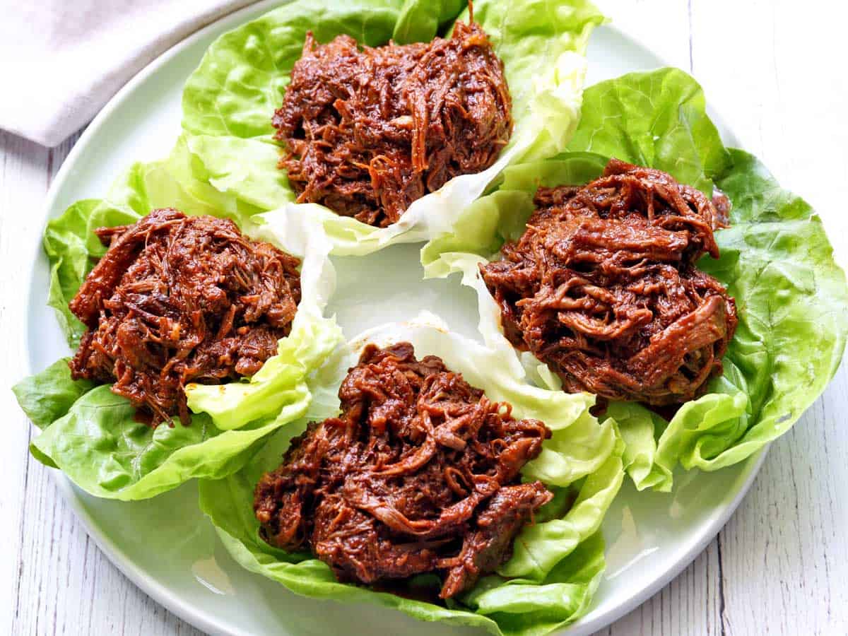Pulled beef served on a white plate in lettuce wraps. 