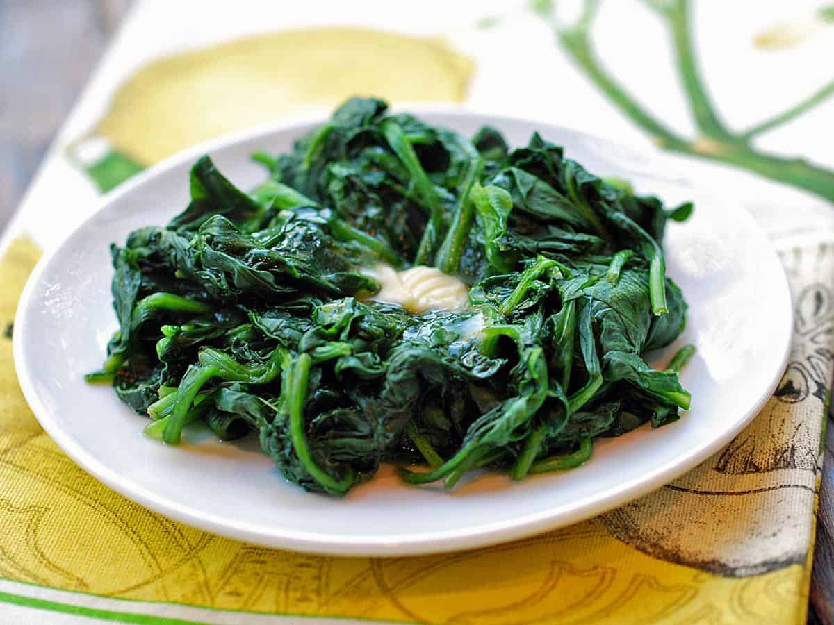 Steamed Spinach topped with butter, served on a white plate. 