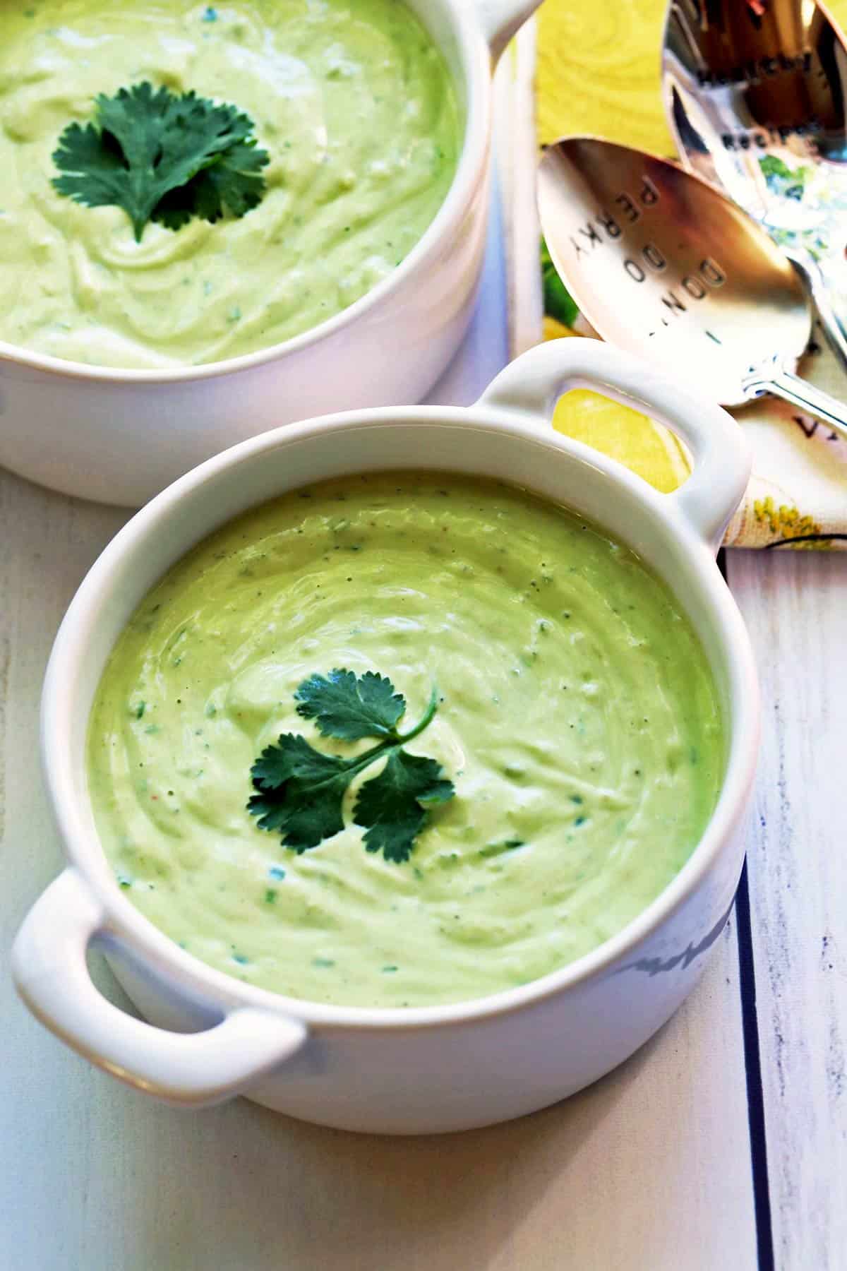 Two bowls of avocado soup garnished with cilantro. 
