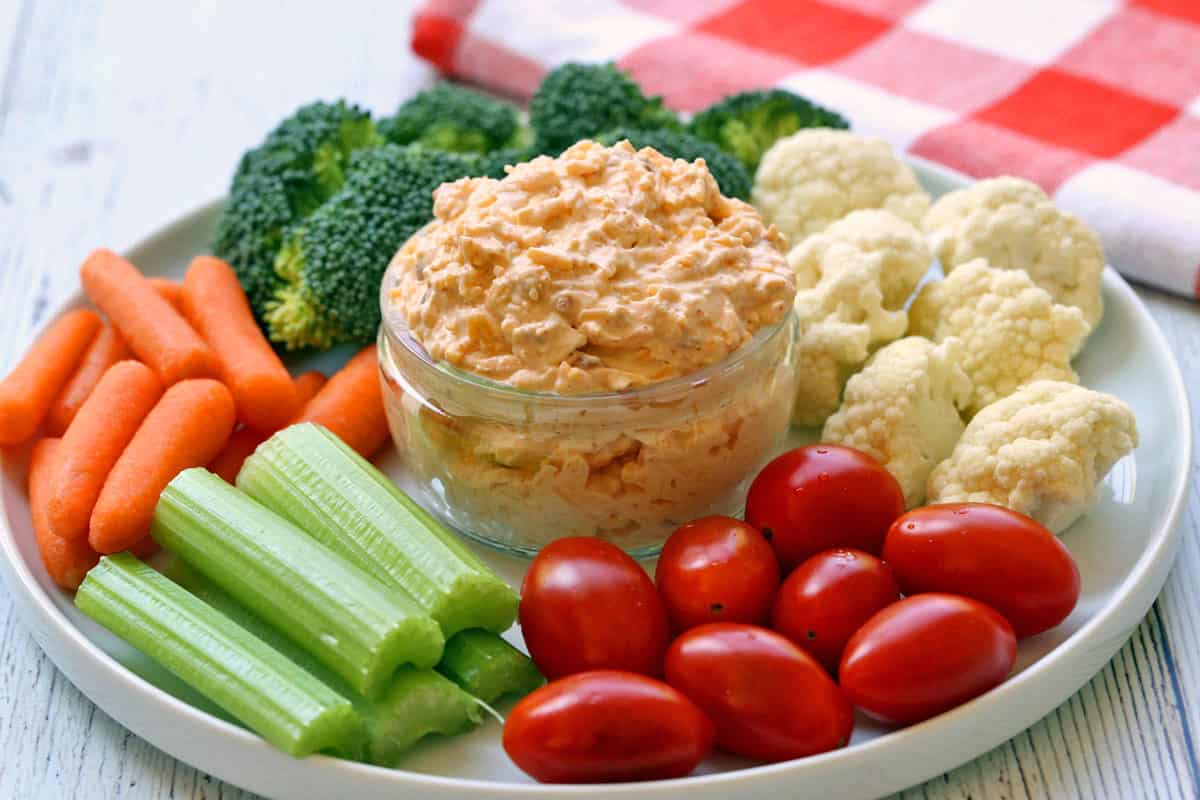 Cream cheese dip is served in a white bowl surrounded with fresh-cut veggies. 
