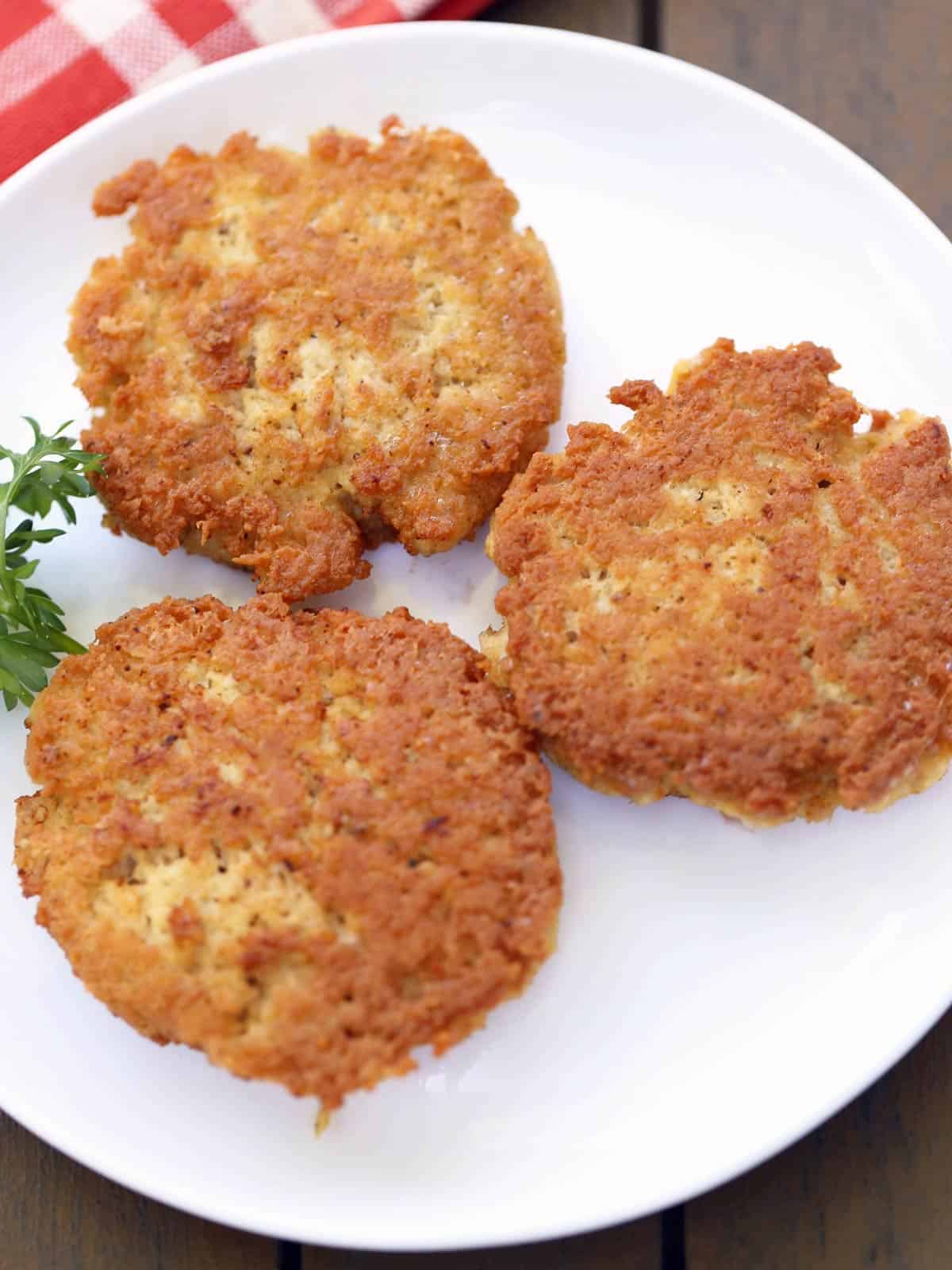 Three chicken patties served on a white plate with a red napkin. 