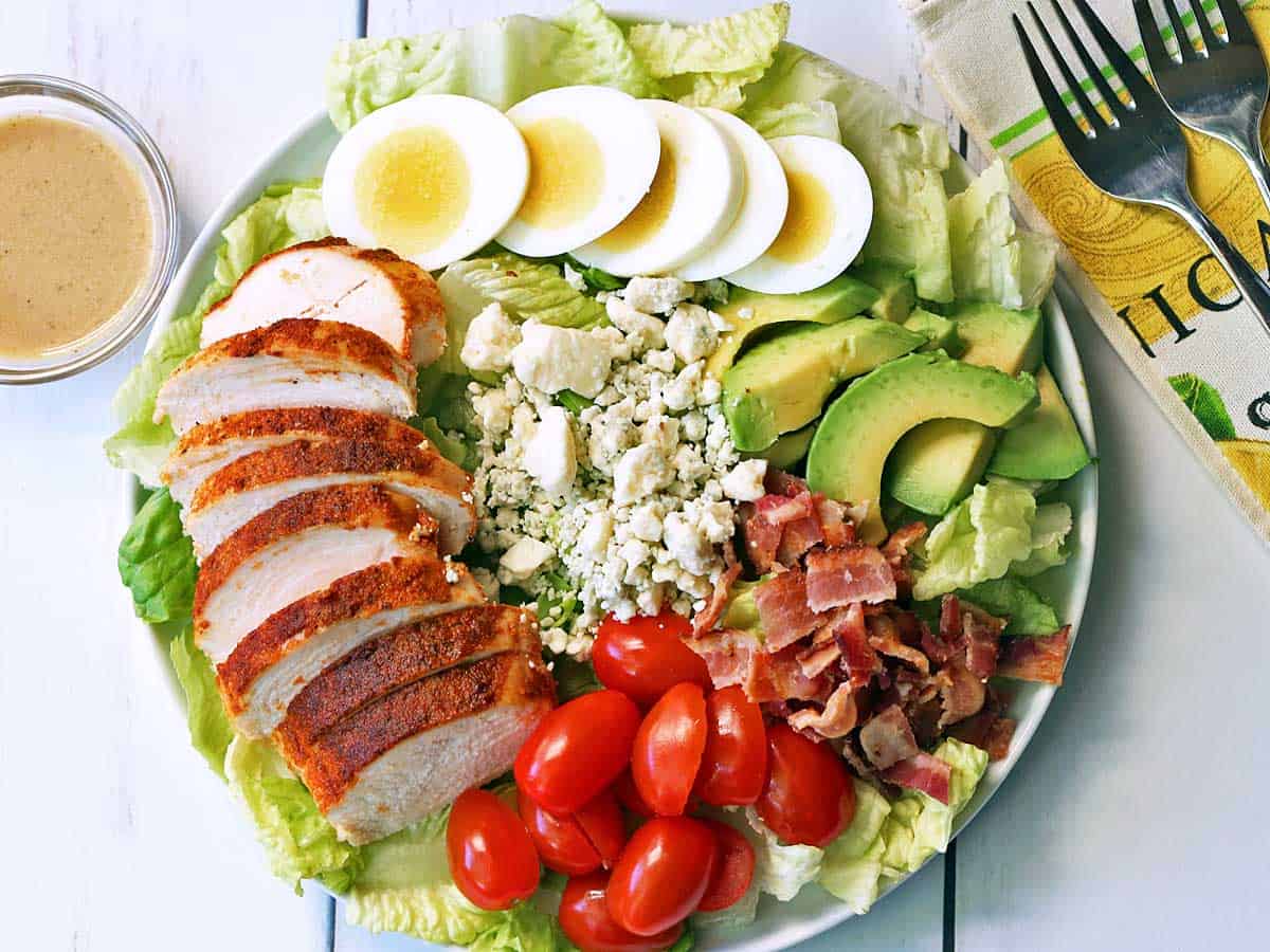 Cobb salad served on a white plate with dressing on the side. 