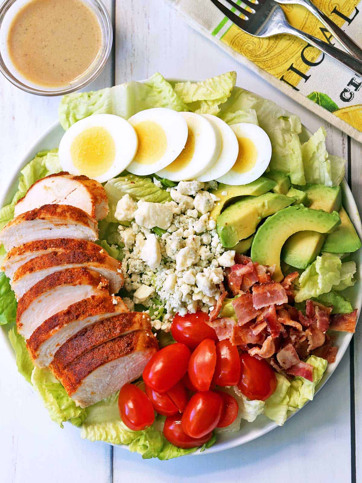 Chicken Cobb salad served on a white plate with a napkin and dressing on the side. 