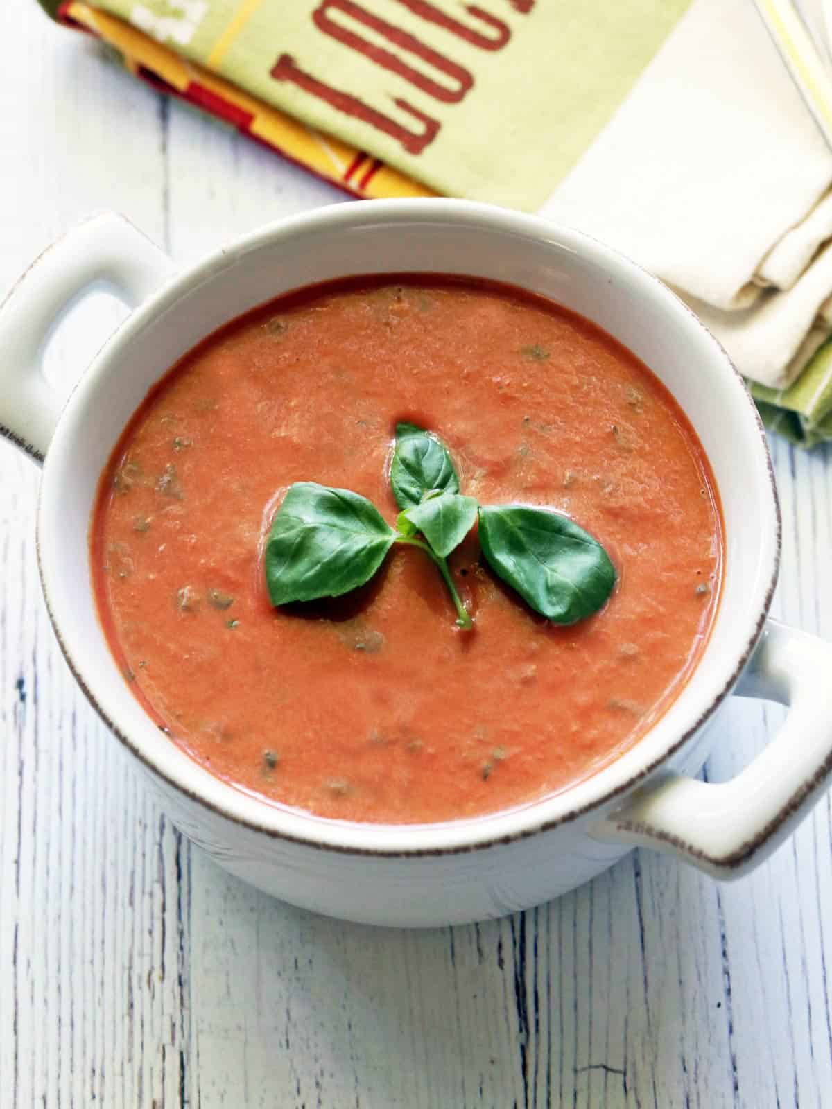 Sopa fría de tomate servida en un tazón blanco, adornada con albahaca. 