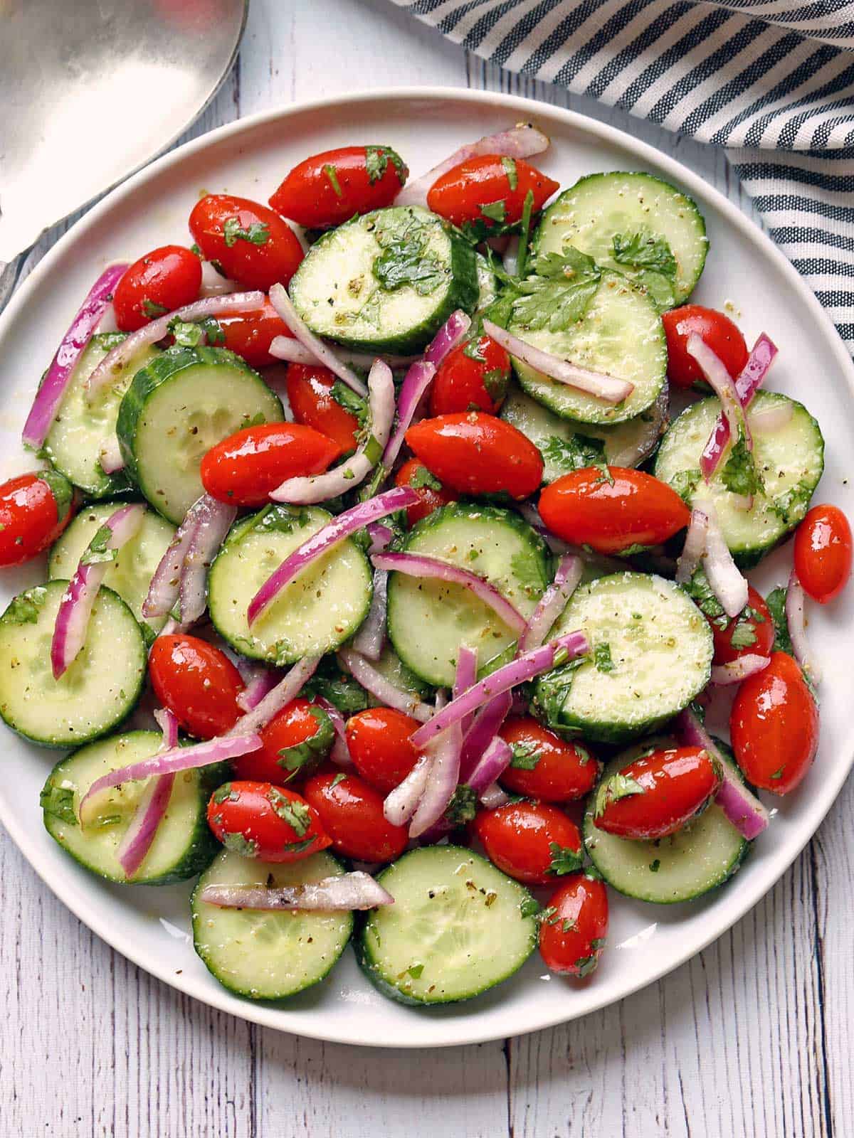 Cucumber tomato salad served on a white plate with a serving spoon. 