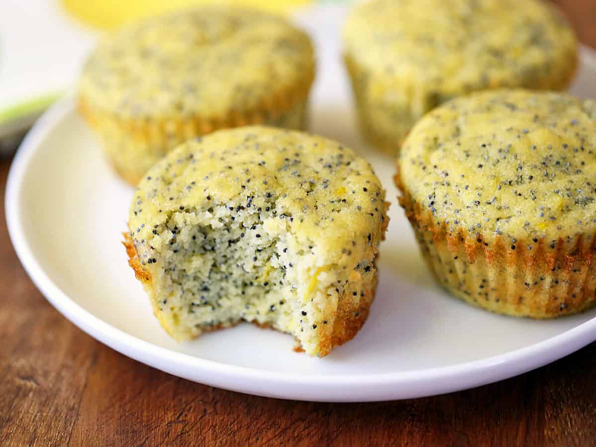 Four keto lemon poppy seed muffins served on a white plate. 