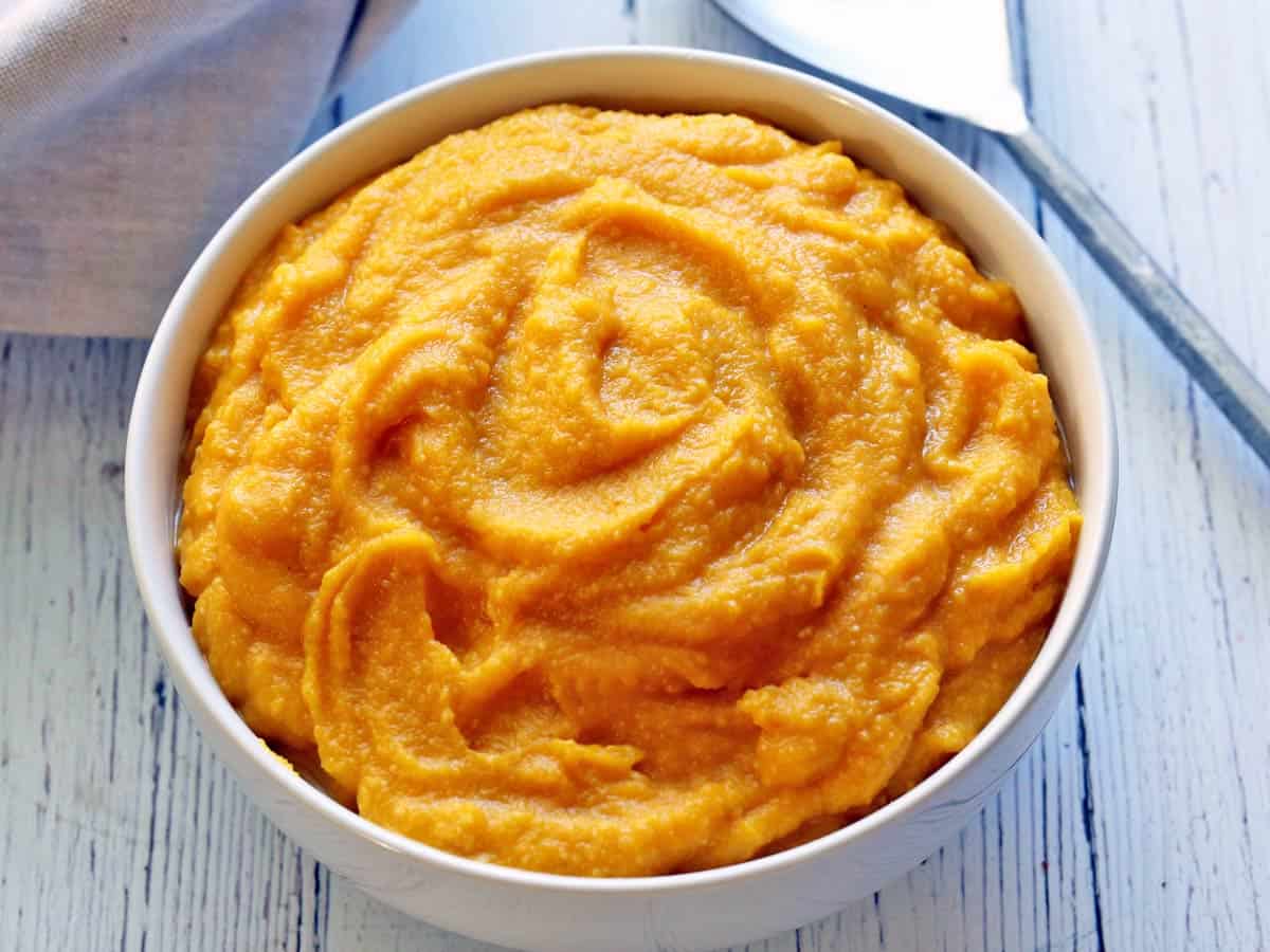 Mashed pumpkin served in a white bowl with a serving spoon. 