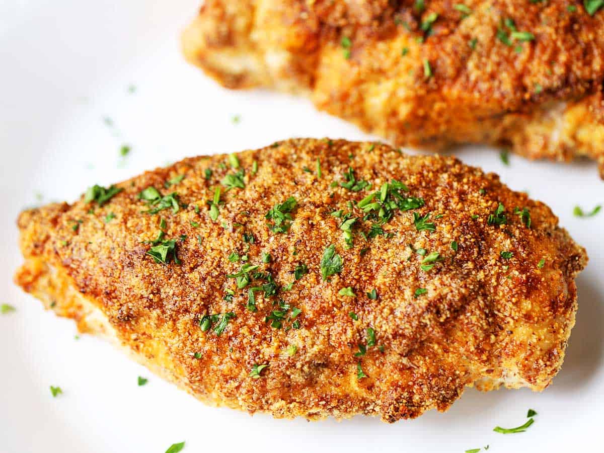 Two pieces of parmesan-crusted chicken served on a white plate. 