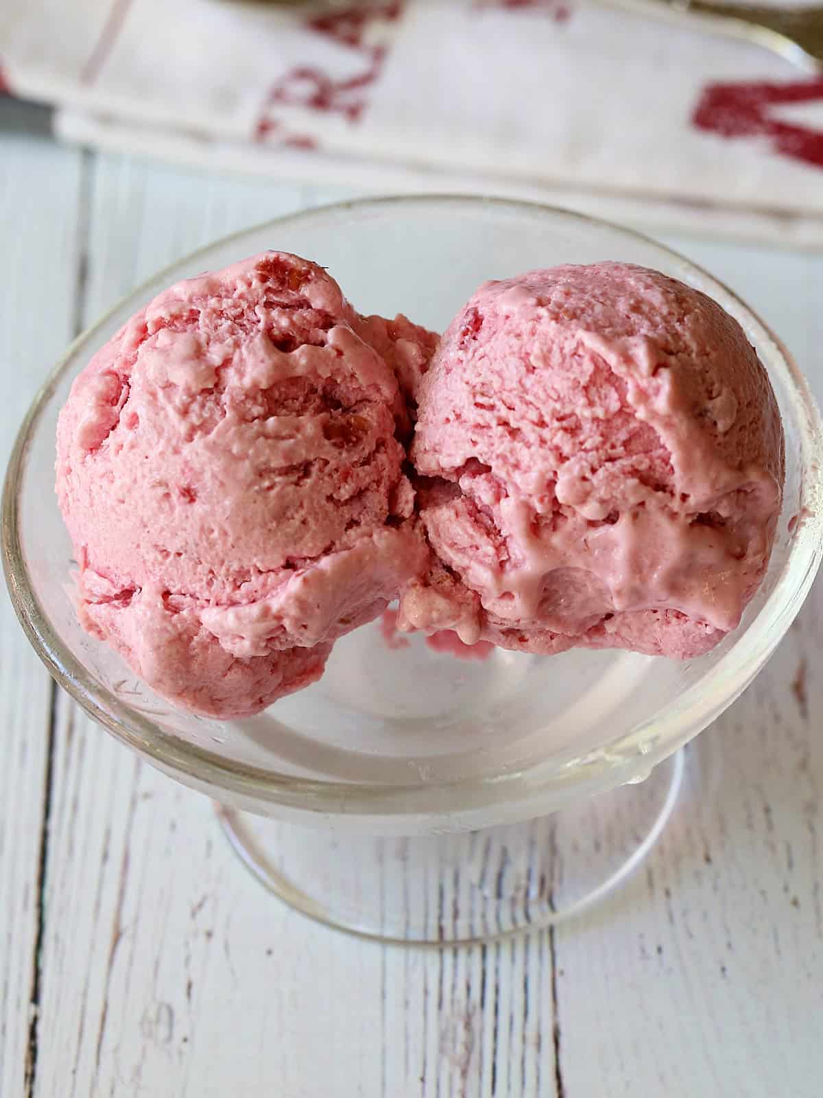 Two scoops of raspberry frozen yogurt served in a glass dessert bowl. 
