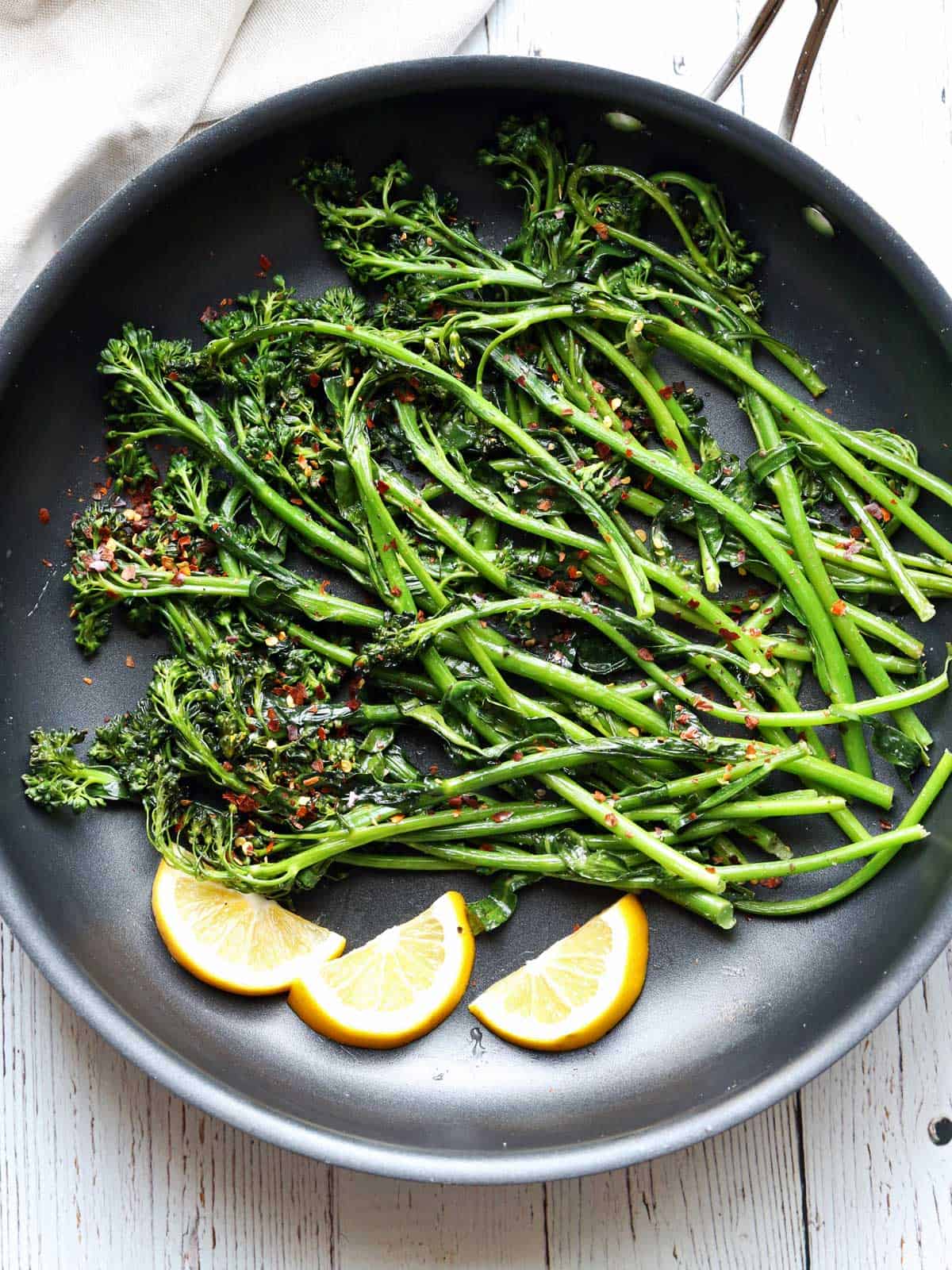 Sauteed broccolini is served with lemon slices.