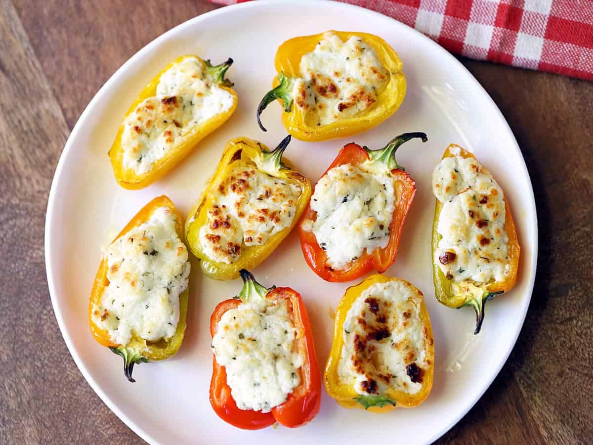 Stuffed mini peppers served on a white plate with a checkered red-and-white napkin. 