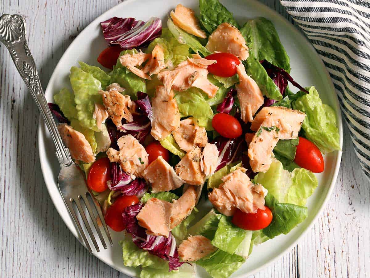 Using up leftover salmon in a salad. The salad contains lettuce and tomatoes and is served on a white plate. 