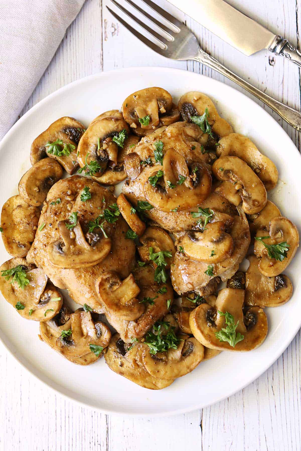 Chicken and mushrooms served on a white plate with utensils and a napkin. 