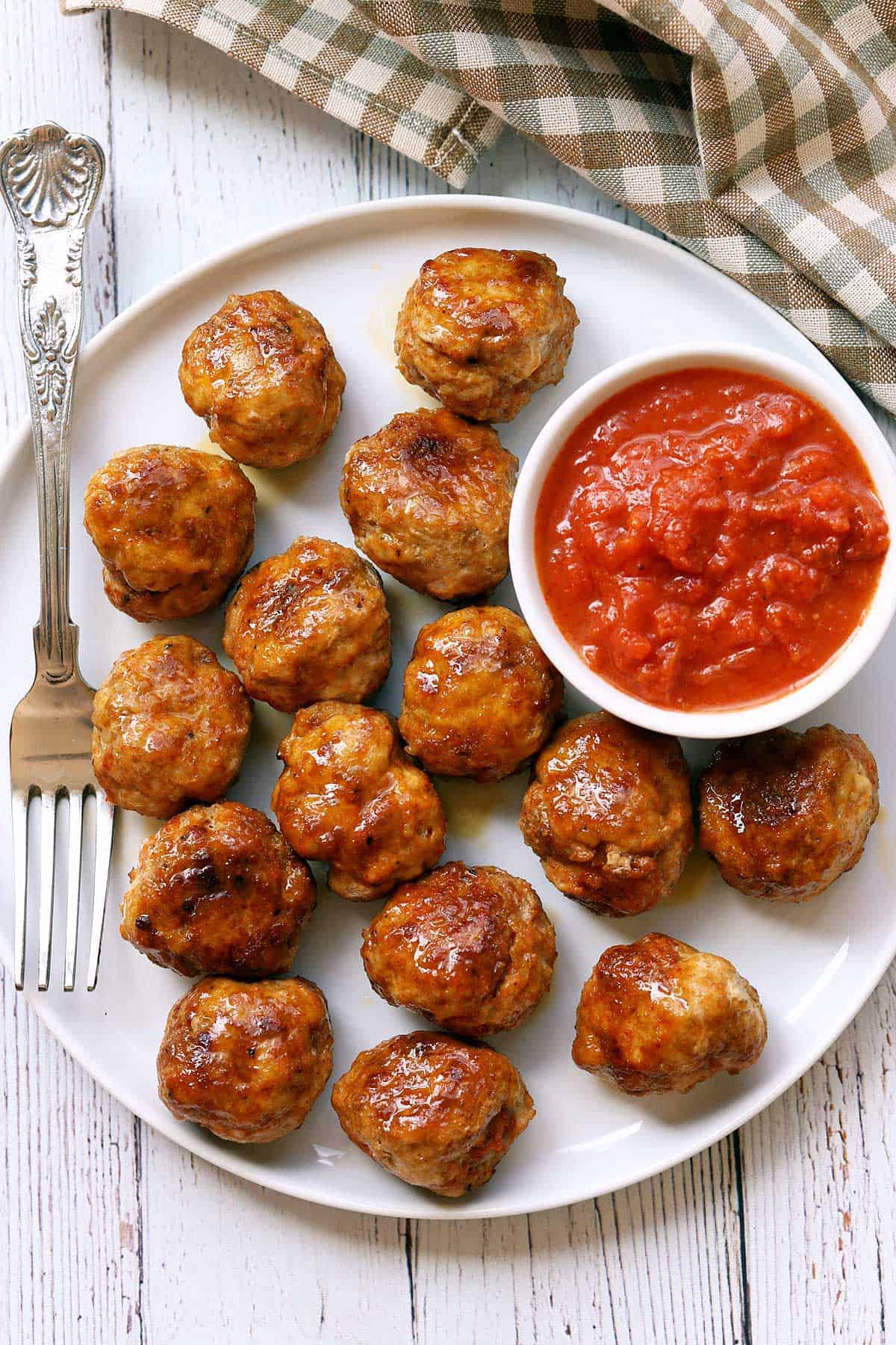 Chicken meatballs served on a white plate with a silver fork and a dipping sauce. 