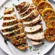 Greek chicken, sliced and served with lemon slices.