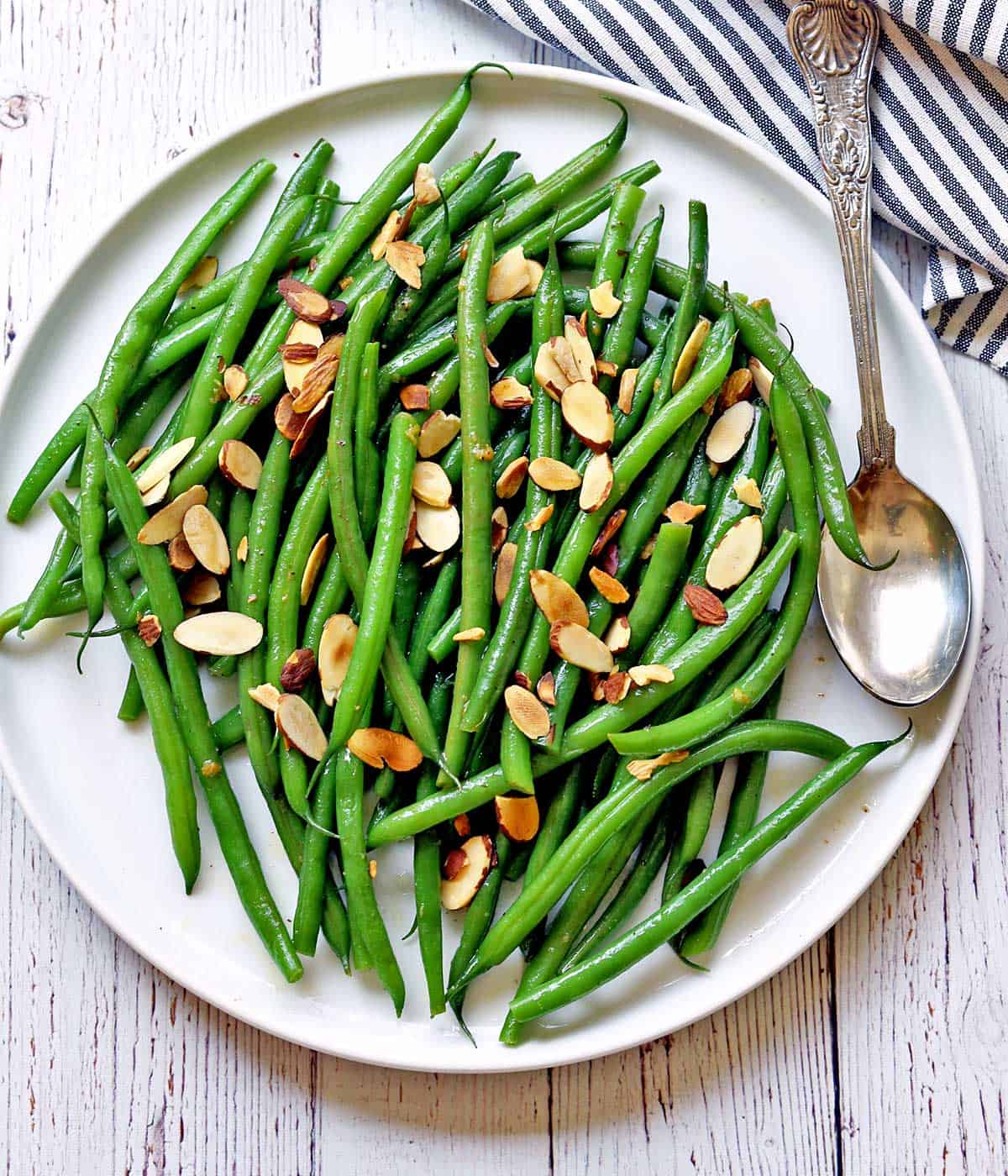 Green beans almondine served on a white plate with a serving spoon. 