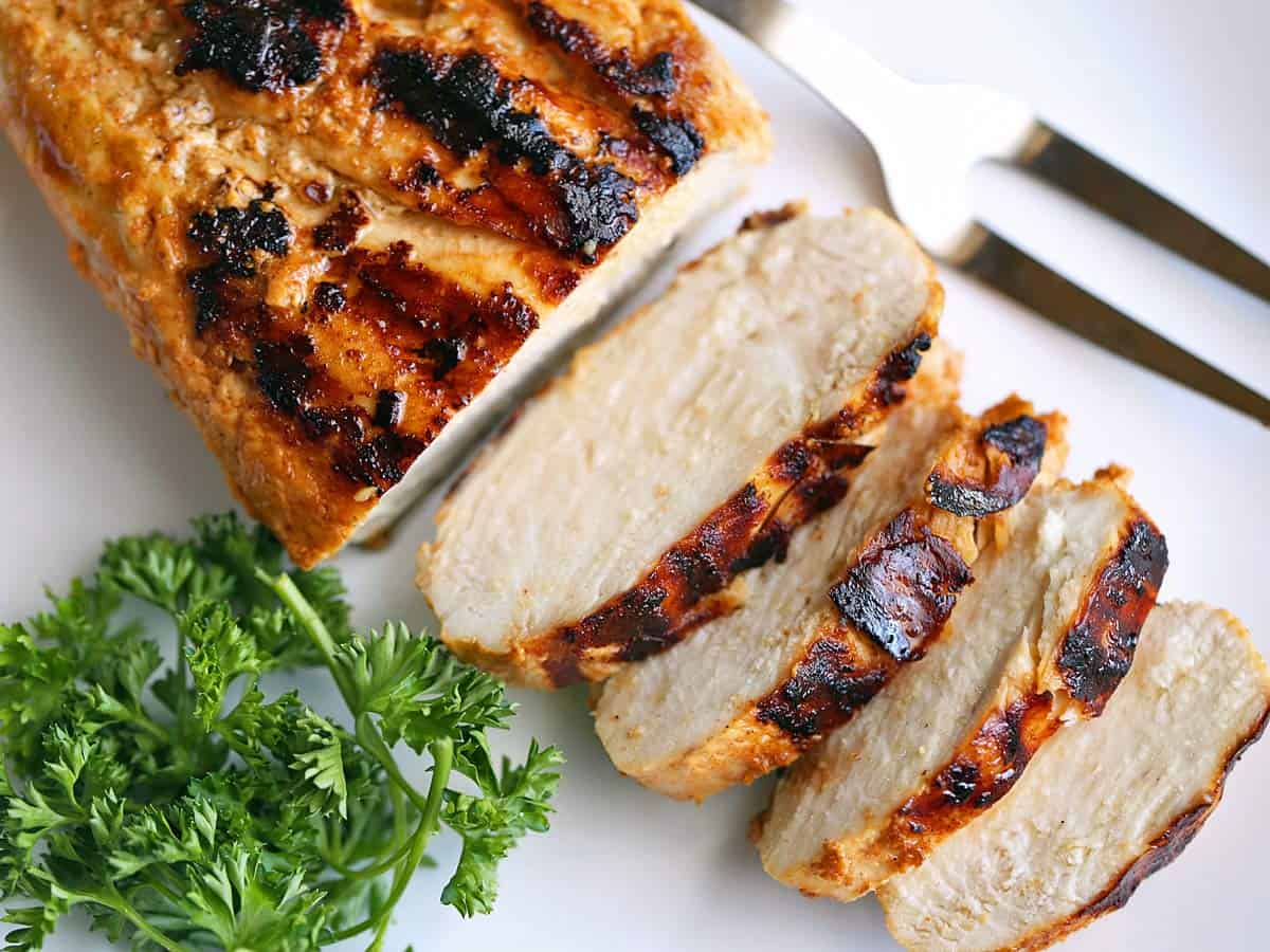 Grilled chicken breast served on a white plate with a serving fork. 