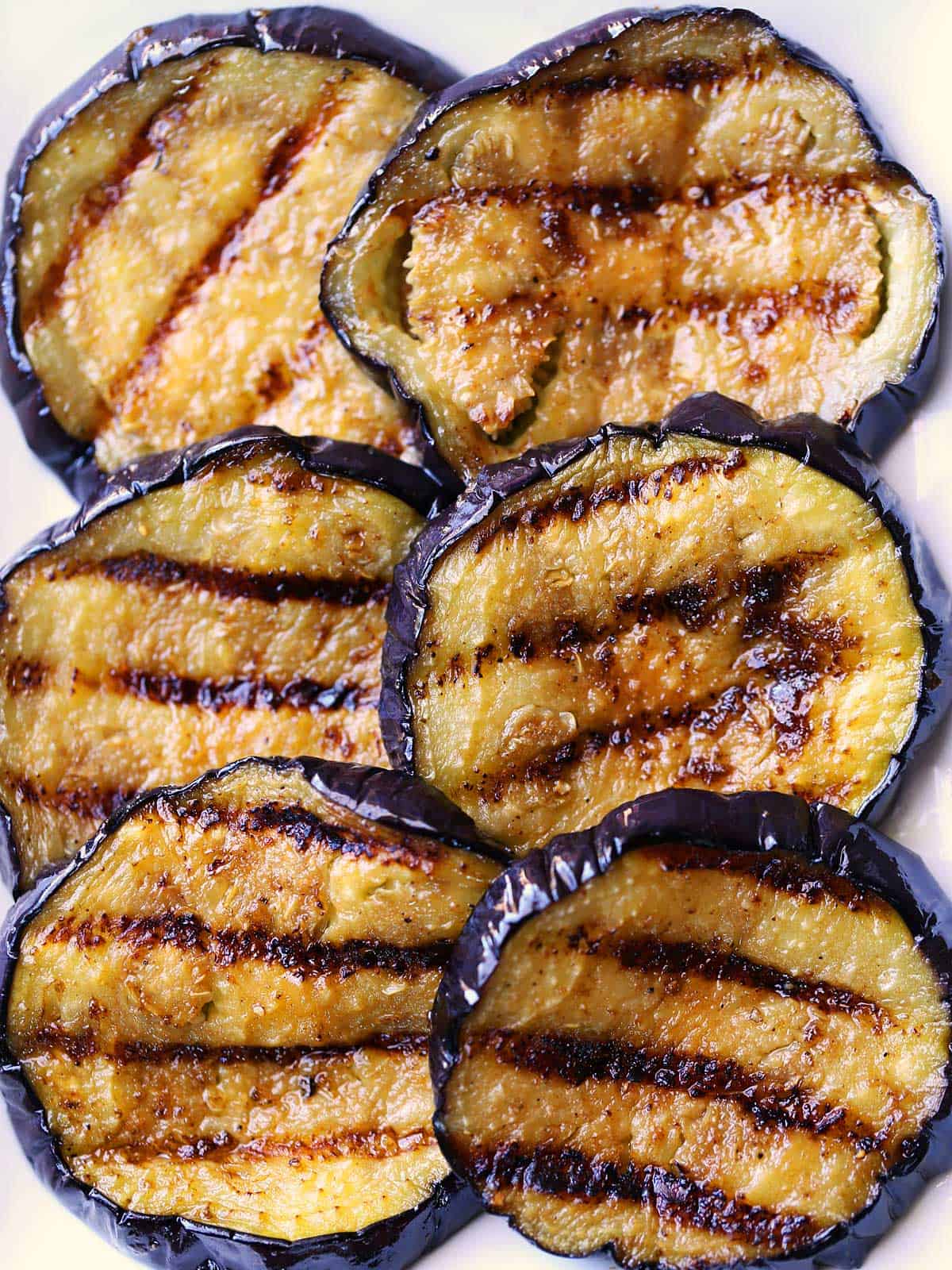 Six grilled eggplant slices served on a white plate. 