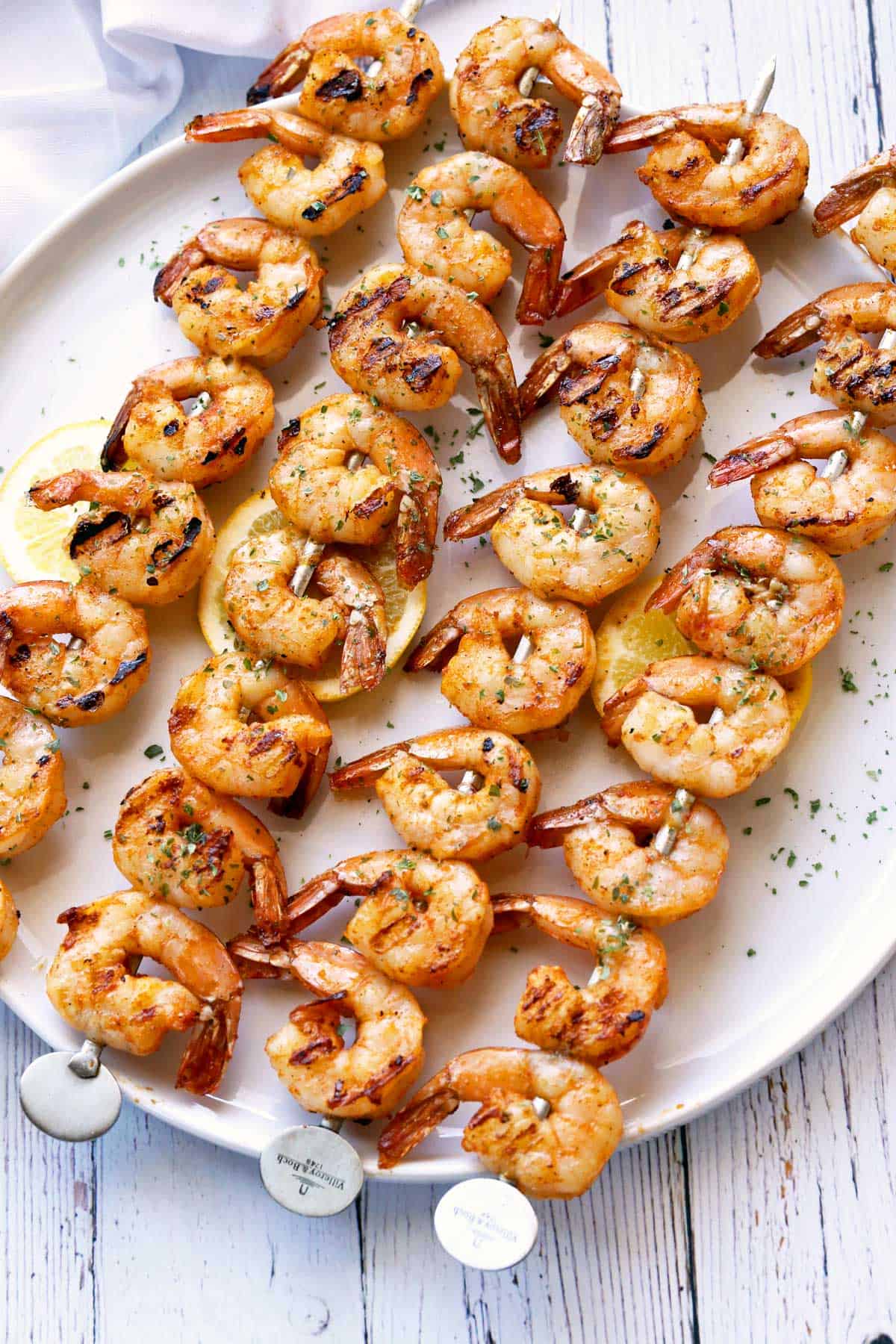 Grilled shrimp threaded on skewers, served on a white plate with a napkin. 