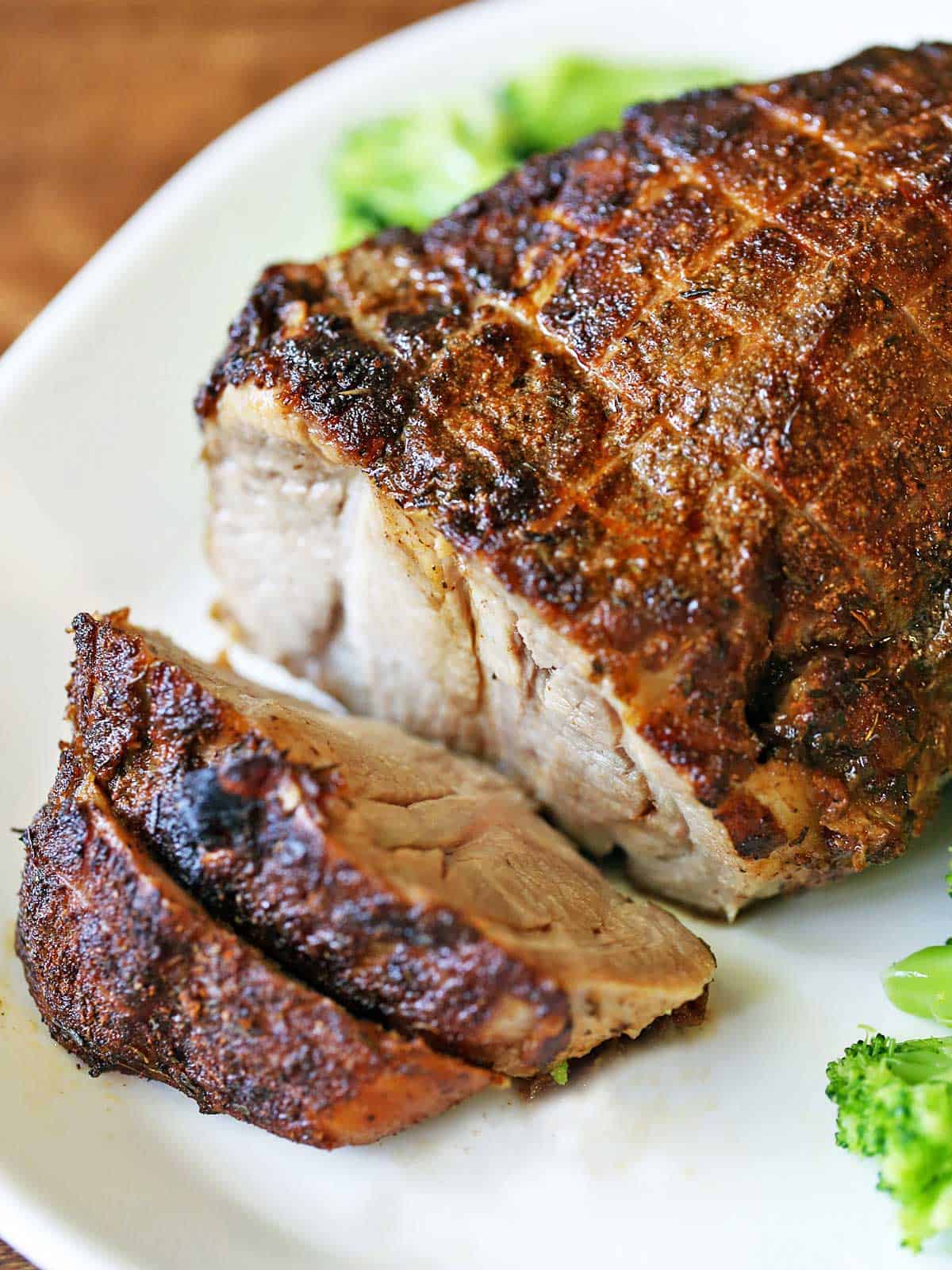 Oven-baked boneless pork roast served on a white platter with veggies.