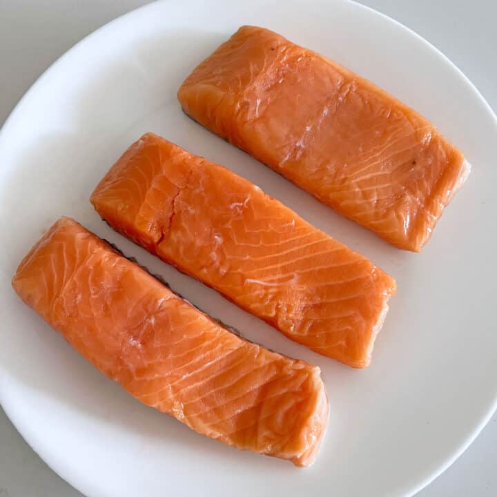 Three salmon fillets on a plate. They don't have bones.