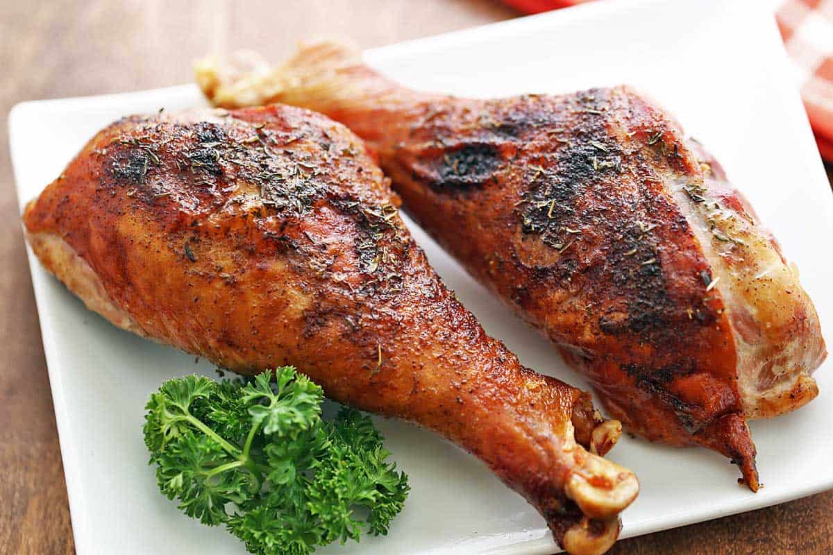 Two roasted turkey legs are served on a white plate with a garnish of parsley. 