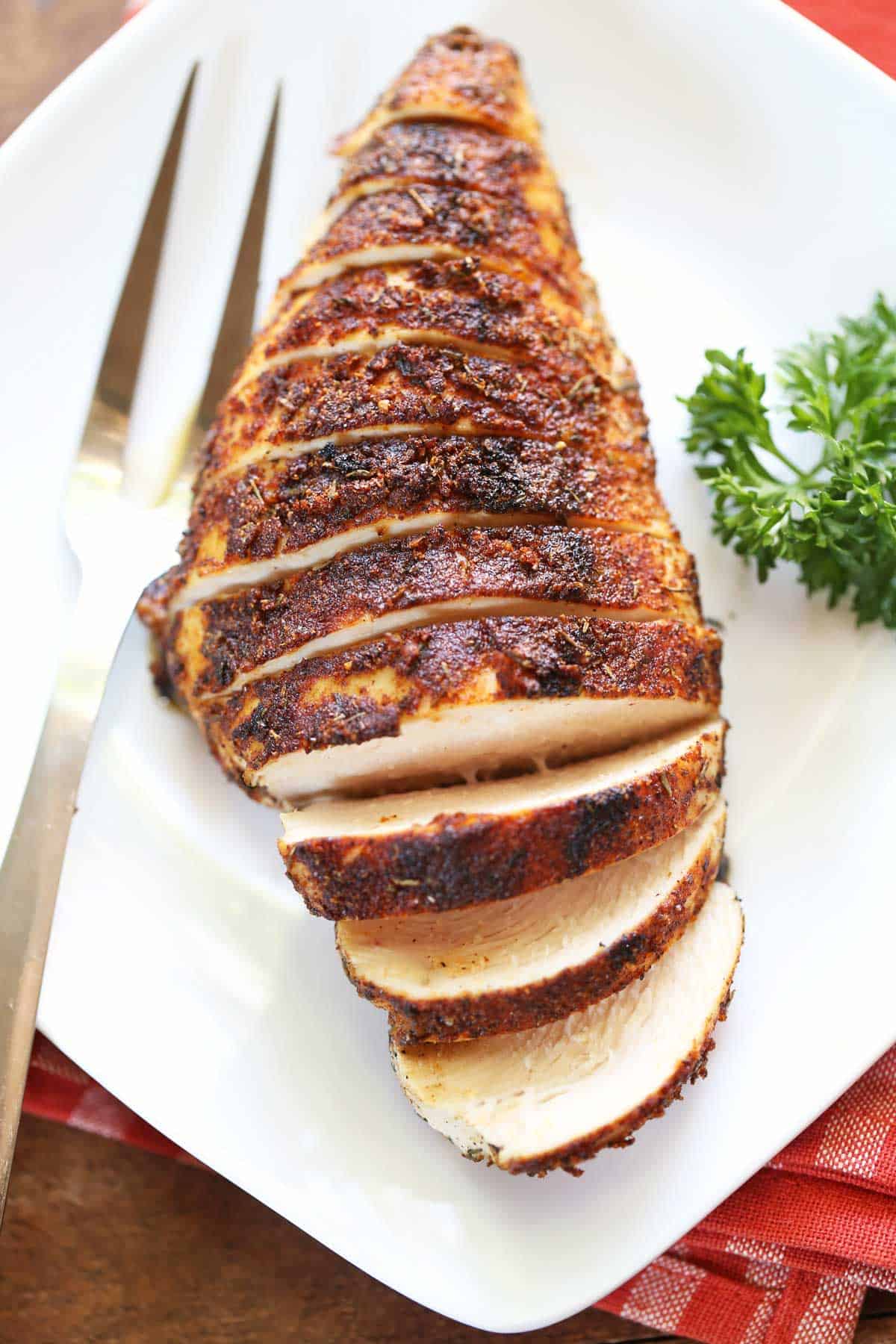 Blackened chicken, sliced and served on a white platter with a serving fork. 
