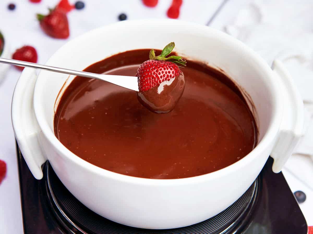 Chocolate fondue served in a white fondue pot with strawberries.