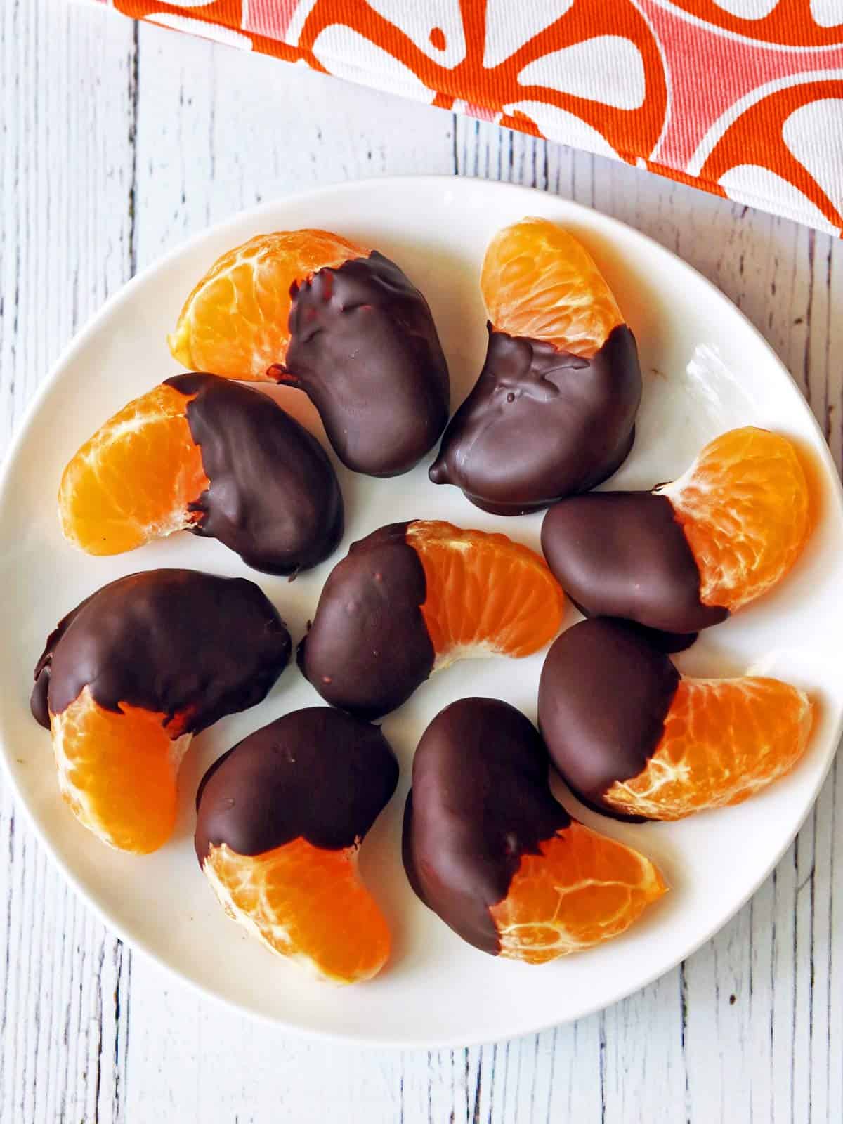 Chocolate-dipped oranges served on a white plate with a napkin. 