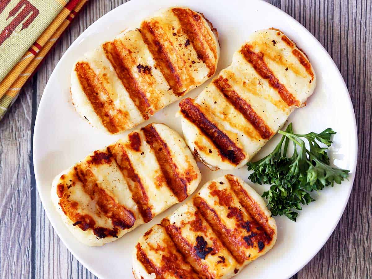 Four pieces of grilled halloumi cheese served on a white plate. 