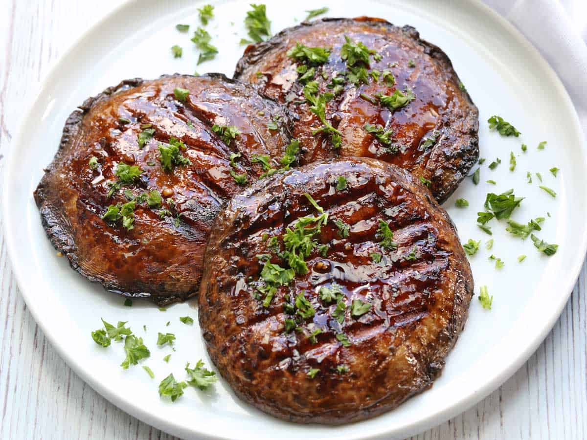 Three grilled portobello mushrooms served on a white plate. 