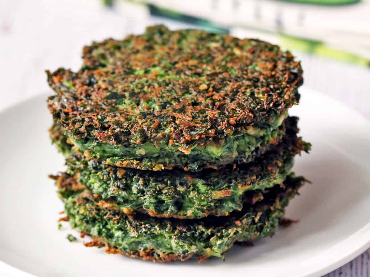 Three kale fritters stacked on a white plate. 