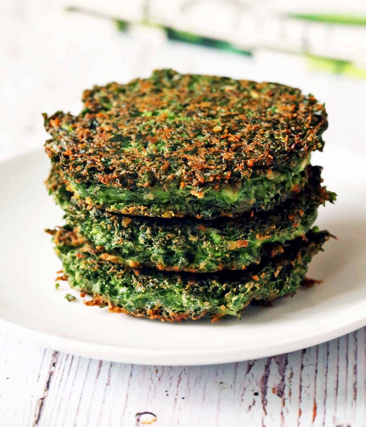 Three kale fritters stacked on a plate. 