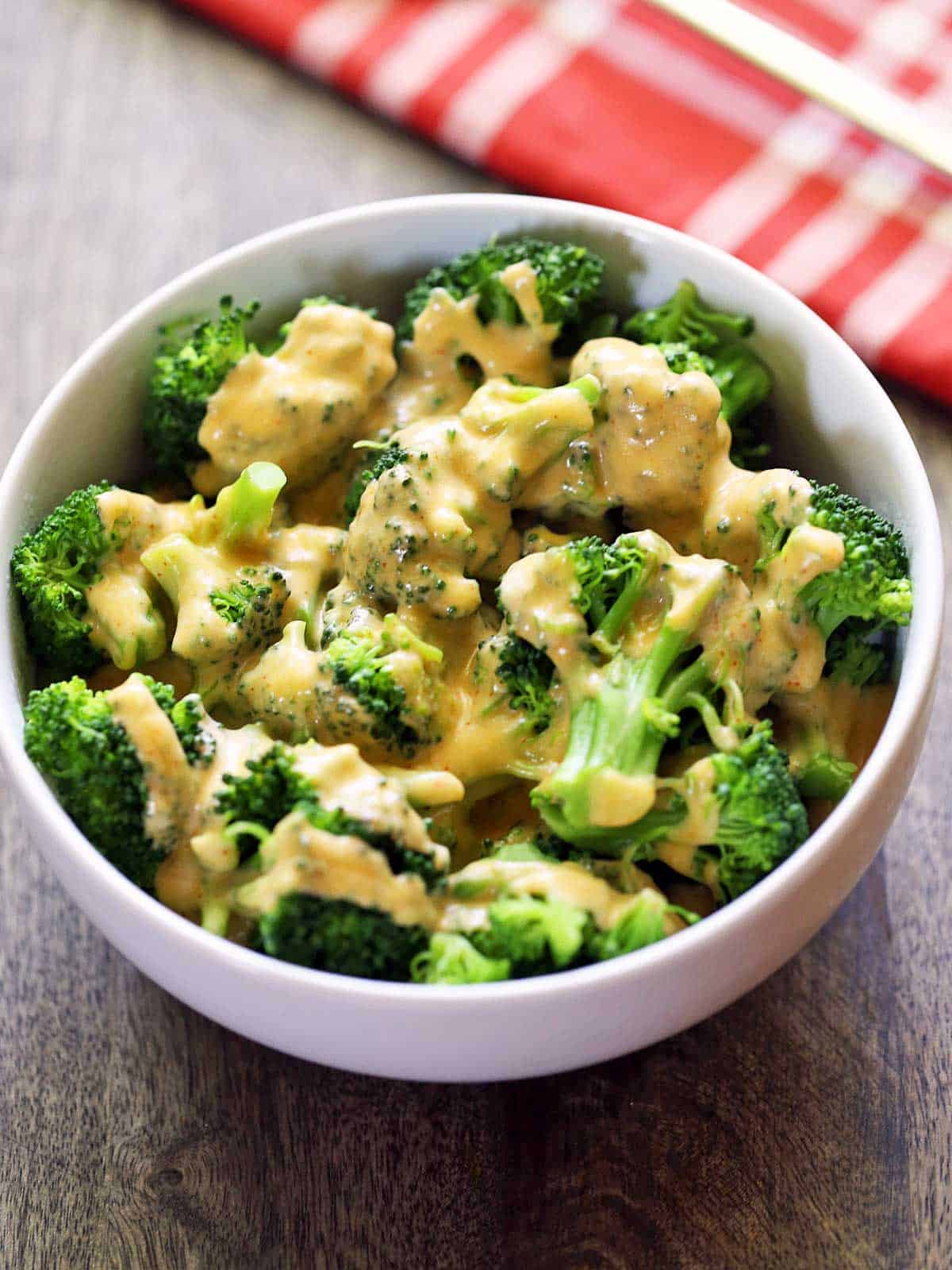 Broccoli served in a white bowl, topped with keto cheese sauce. 