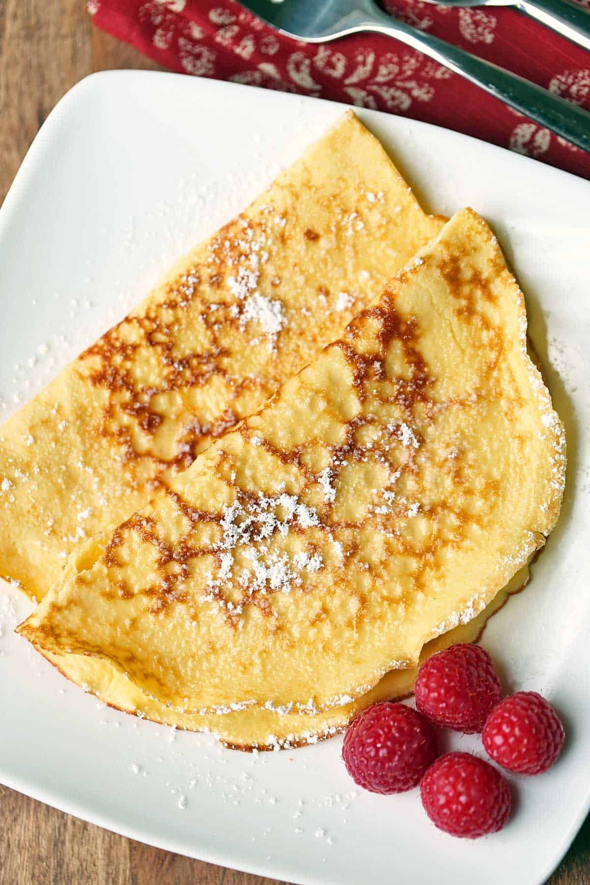 Two keto crepes served on a white plate garnished with raspberries. 